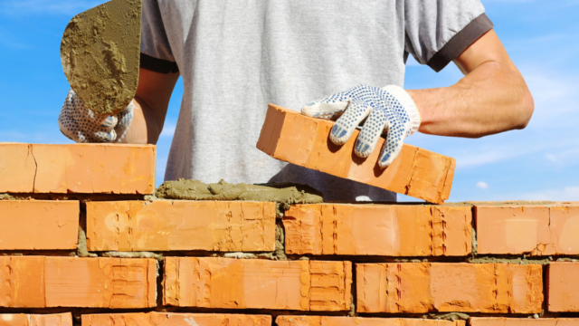 a man's hands laying brick on to a wall with a blue sky background