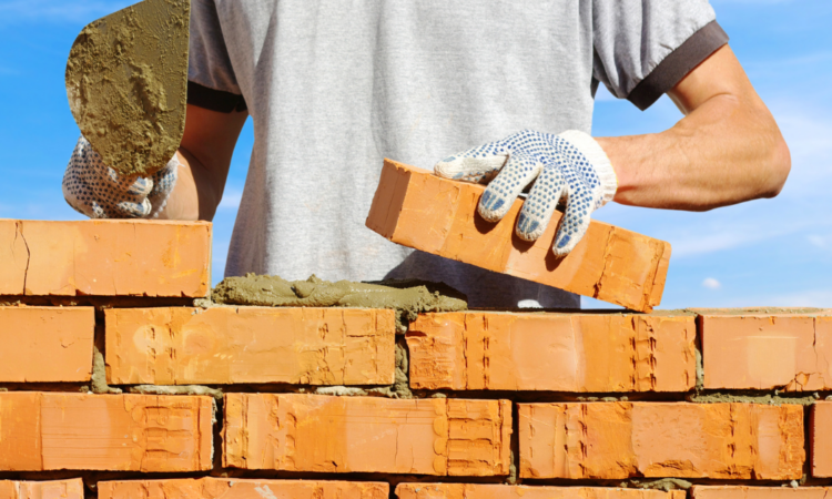 a man's hands laying brick on to a wall with a blue sky background