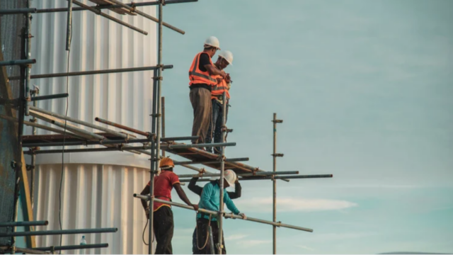 A picture of construction workers standing on a scaffold with the sky in the background