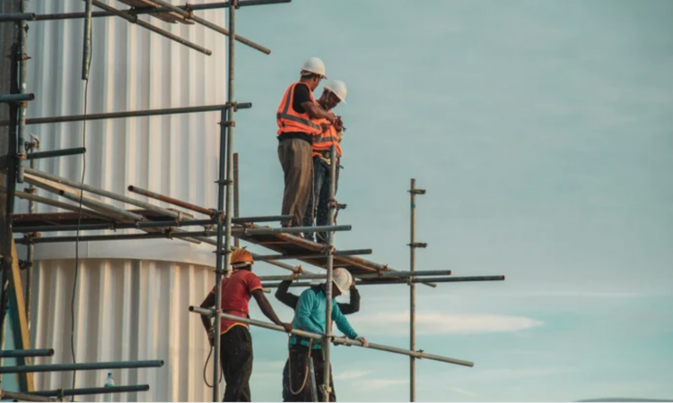 A picture of construction workers standing on a scaffold with the sky in the background
